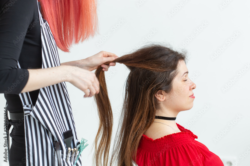Fototapeta premium Hair Stylist, beauty and people concept - female hairdresser coloring young woman.