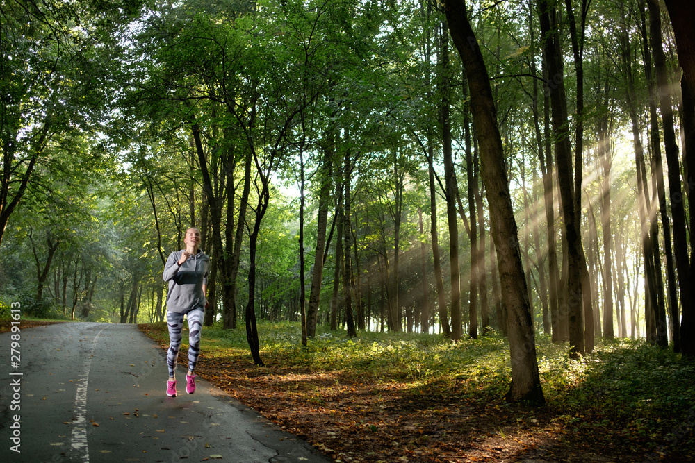 Athletic young woman wearing sportswear running in the park or forest in sunny morning. Right morning. Summer time. Athletic young woman wearing sportswear running in the park or forest in sunny morning. Right morning. Summer time.