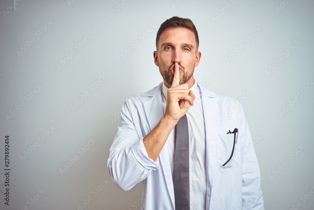 Young handsome doctor man wearing white profressional coat over isolated background asking to be quiet with finger on lips. Silence and secret concept. Young handsome doctor man wearing white profressional coat over isolated background asking to be quiet with finger on lips. Silence and secret concept.