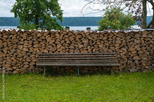 A large woodpile of birch wood and a wooden bench for rest.
