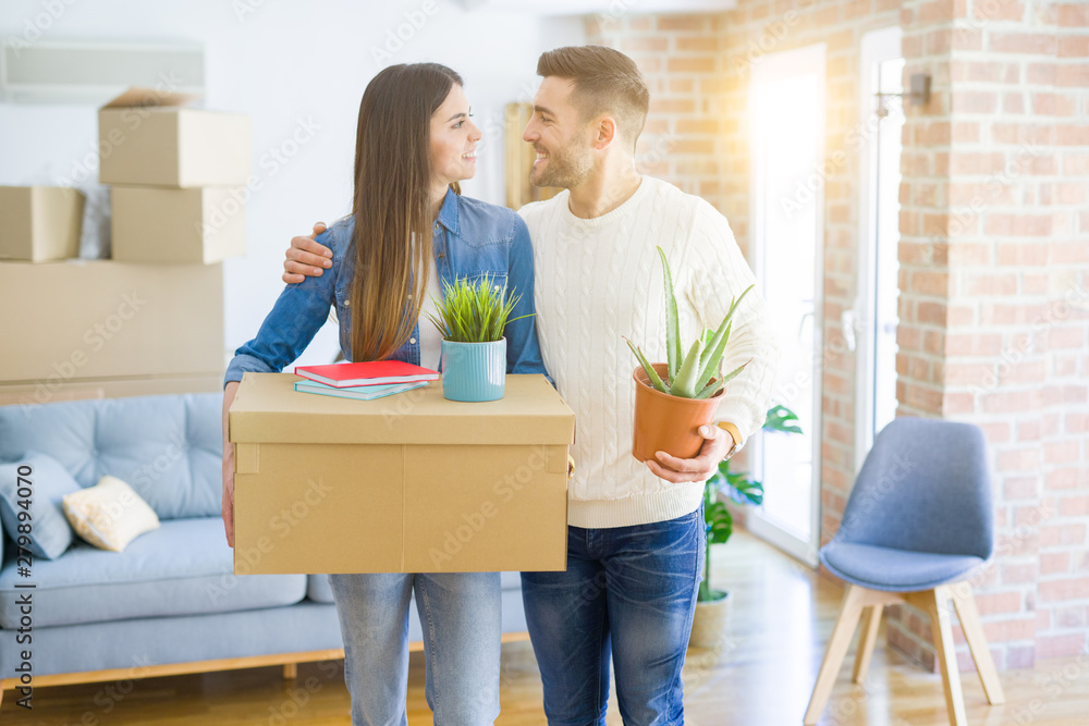 Beautiful young couple moving to a new house, smiling happy holding cardboard boxes at new apartment