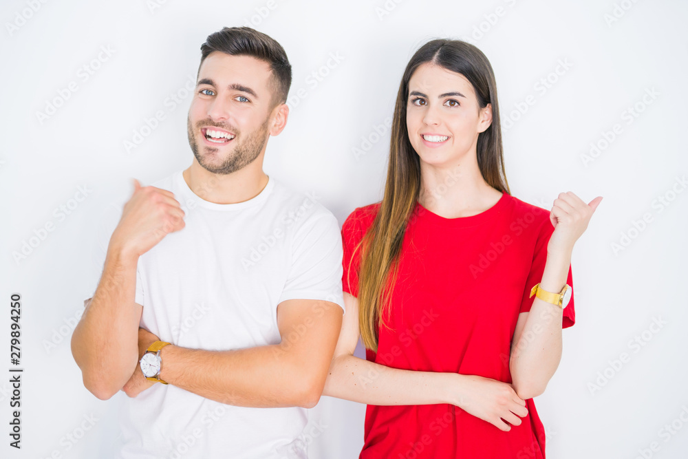 Young beautiful couple together over white isolated background smiling with happy face looking and pointing to the side with thumb up. Young beautiful couple together over white isolated background smiling with happy face looking and pointing to the side with thumb up.