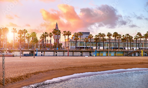 Barcelona, Spain. Panoramic view at Barceloneta beach from sea. View with stones. Sunset landscape with blue sky. Sandy coastline with palms and waves of surf. Popular touristic vacation destination. photo