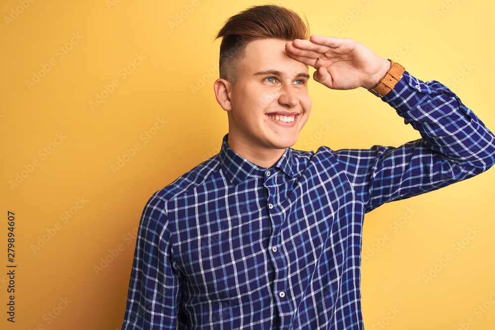 Young handsome man wearing casual shirt standing over isolated yellow background very happy and smiling looking far away with hand over head. Searching concept. Young handsome man wearing casual shirt standing over isolated yellow background very happy and smiling looking far away with hand over head. Searching concept.