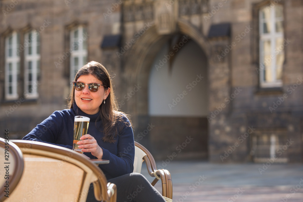 Lady sits at a city cafe outdoors and drinks a glass of beer.
