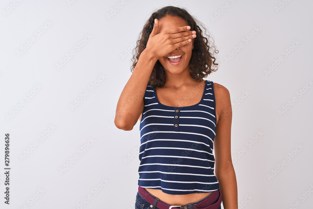 Young brazilian woman wearing striped t-shirt standing over isolated white background smiling and laughing with hand on face covering eyes for surprise. Blind concept. Young brazilian woman wearing striped t-shirt standing over isolated white background smiling and laughing with hand on face covering eyes for surprise. Blind concept.