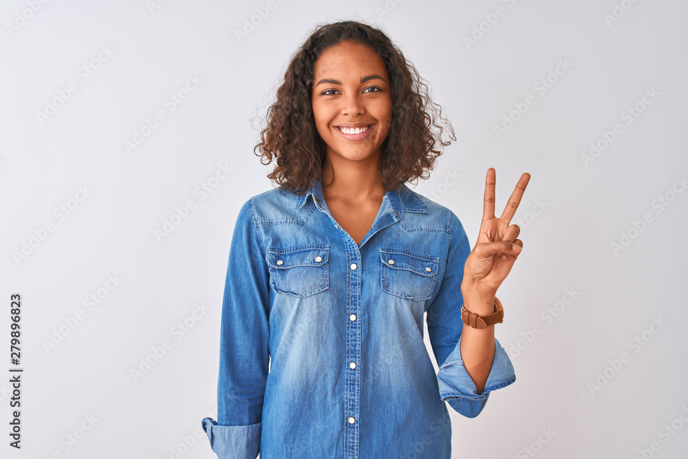 Young brazilian woman wearing denim shirt standing over isolated white background showing and pointing up with fingers number two while smiling confident and happy. Young brazilian woman wearing denim shirt standing over isolated white background showing and pointing up with fingers number two while smiling confident and happy.