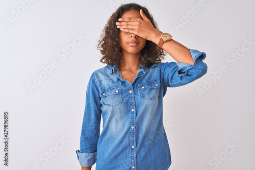 Young brazilian woman wearing denim shirt standing over isolated white background covering eyes with hand, looking serious and sad. Sightless, hiding and rejection concept