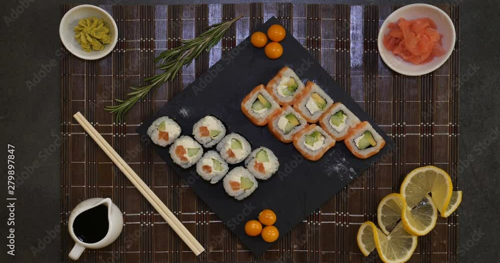 Served A Set Of Sushi With Salmon And Tuna, California Rolls, Maki, Soy Sauce Closeup On The Table. Hands eat sushi with chopsticks. Served A Set Of Sushi With Salmon And Tuna, California Rolls, Maki, Soy Sauce Closeup On The Table. Hands eat sushi with chopsticks.