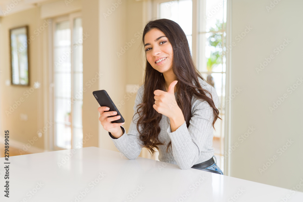 Young woman using smartphone sending a message happy with big smile doing ok sign, thumb up with fingers, excellent sign Young woman using smartphone sending a message happy with big smile doing ok sign, thumb up with fingers, excellent sign
