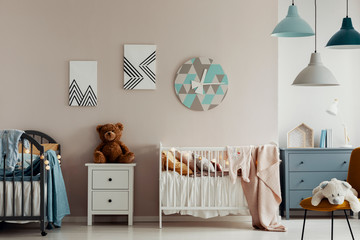 A teddy bear, two beds and a large clock on a beige wall in bright and warm bedroom interior for twins. Real photo
