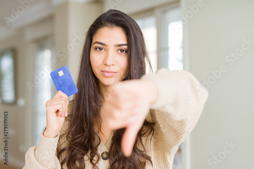 Young woman holding credit card as payment with angry face, negative sign showing dislike with thumbs down, rejection concept