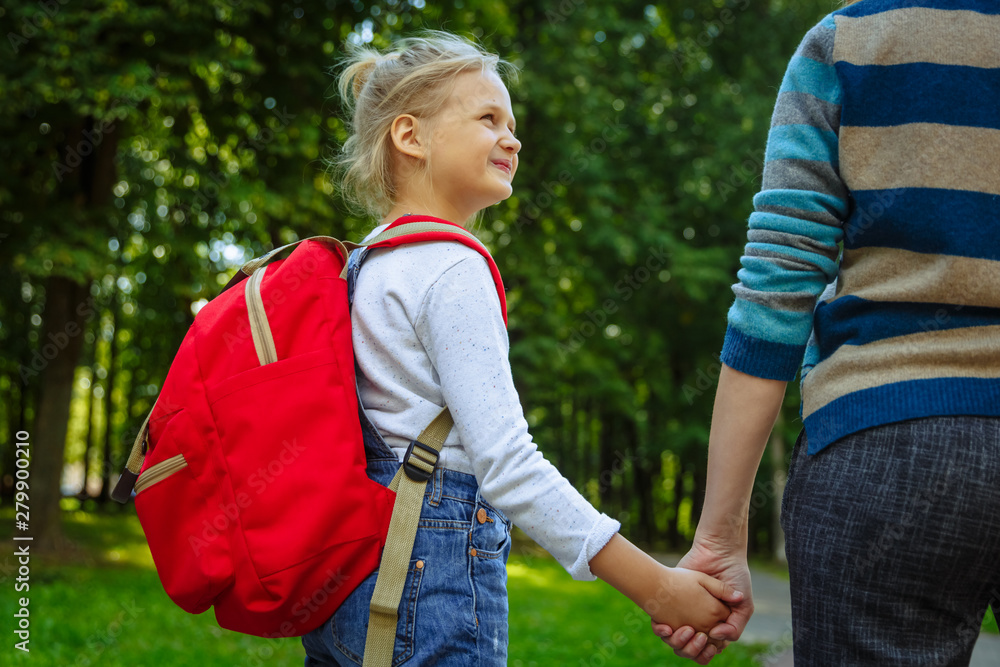 First day at school. Woman and girl with red backpack behind the back. Beginning of lessons. First day of fall. Back to school concept. First day at school. Woman and girl with red backpack behind the back. Beginning of lessons. First day of fall. Back to school concept.