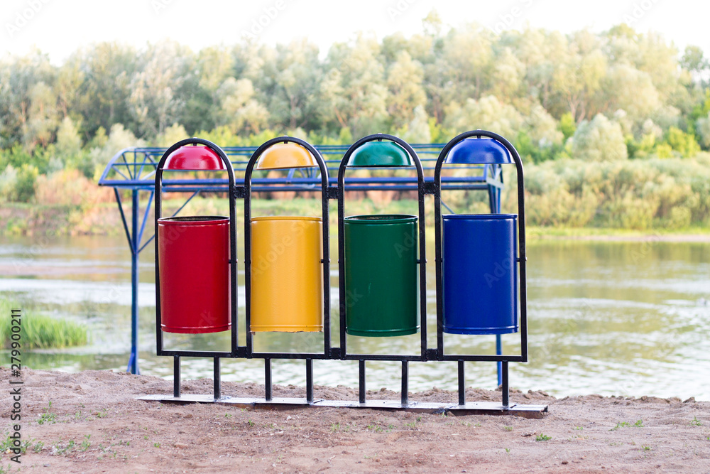 four multi-colored garbage containers stand on the beach by the river near the forest four multi-colored garbage containers stand on the beach by the river near the forest