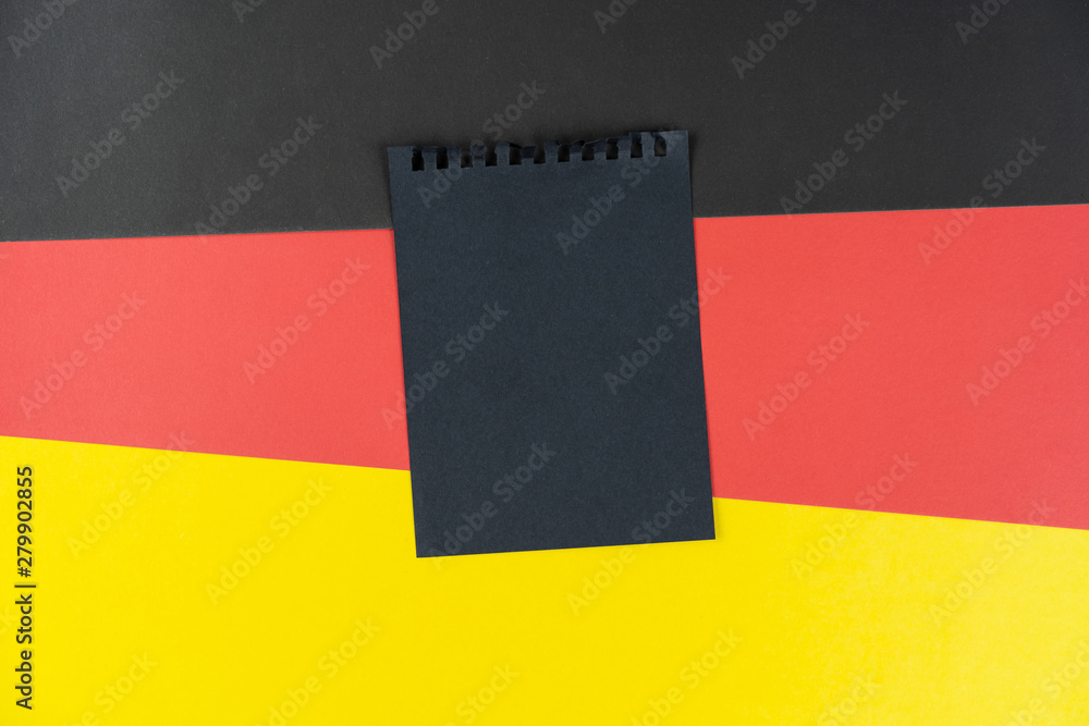 Fototapeta premium Blacklist Germany. Mourning, ban, sanctions, politics. black sheet of notebook lies on German flag. Mock up, copy space, pattern, cardboard texture.