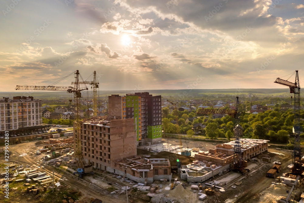 Fototapeta premium Aerial view of building site. Apartment or office building under construction. Tower cranes on suburb landscape and blue sky copy space background.