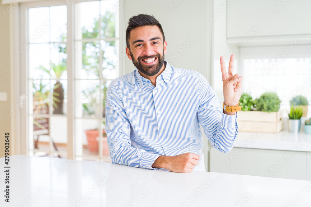 Handsome hispanic business man smiling with happy face winking at the camera doing victory sign. Number two.