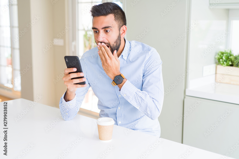 Handsome hispanic business man drinking coffee and using smartphone cover mouth with hand shocked with shame for mistake, expression of fear, scared in silence, secret concept Handsome hispanic business man drinking coffee and using smartphone cover mouth with hand shocked with shame for mistake, expression of fear, scared in silence, secret concept