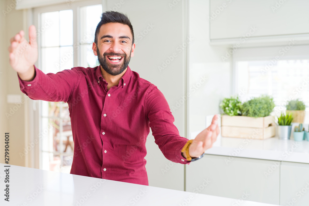 Handsome hispanic business man looking at the camera smiling with open arms for hug. Cheerful expression embracing happiness.