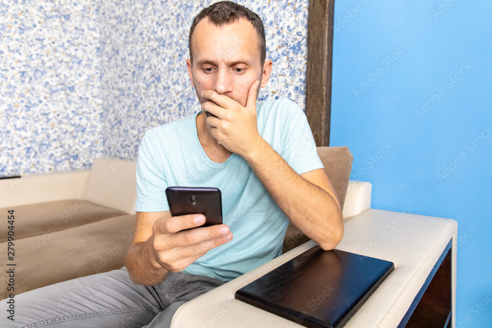 a young man with stunned and fear looks into the screen of a smartphone a young man with stunned and fear looks into the screen of a smartphone