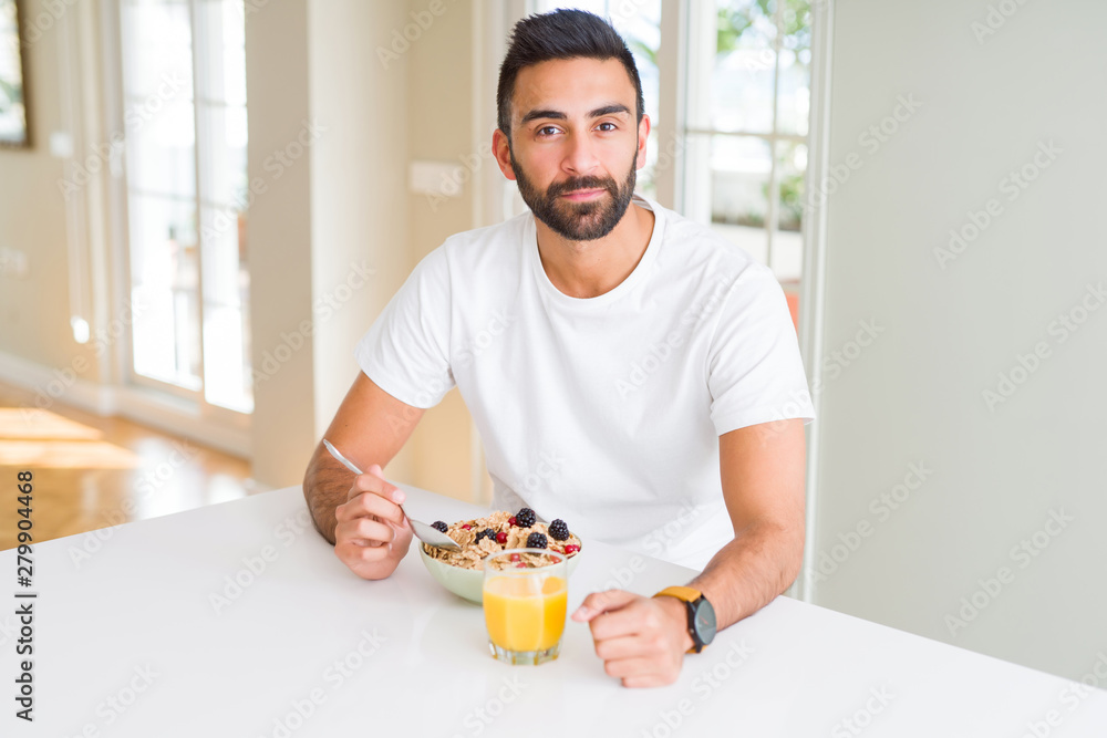 Handsome hispanic man eating healthy breakfast in the morning at home with a confident expression on smart face thinking serious Handsome hispanic man eating healthy breakfast in the morning at home with a confident expression on smart face thinking serious