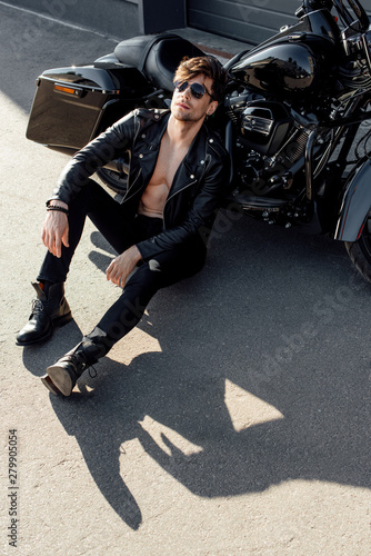 young man relaxing while sitting on ground near black motorcycle