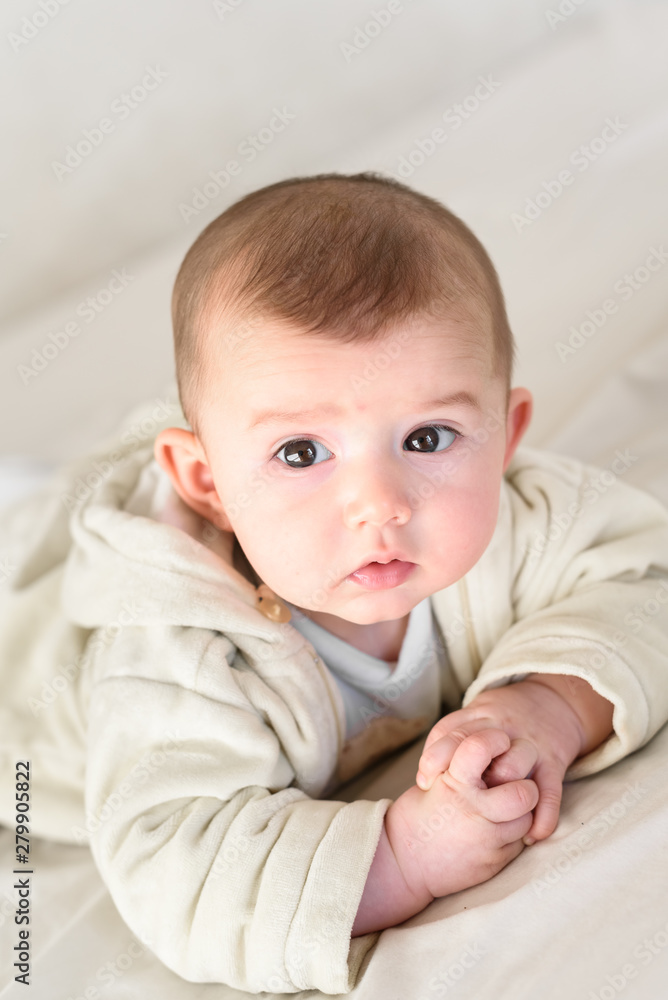 Beautiful and sweet newborn baby lying face down on the bed raising his head to look at the camera curiously. Beautiful and sweet newborn baby lying face down on the bed raising his head to look at the camera curiously.