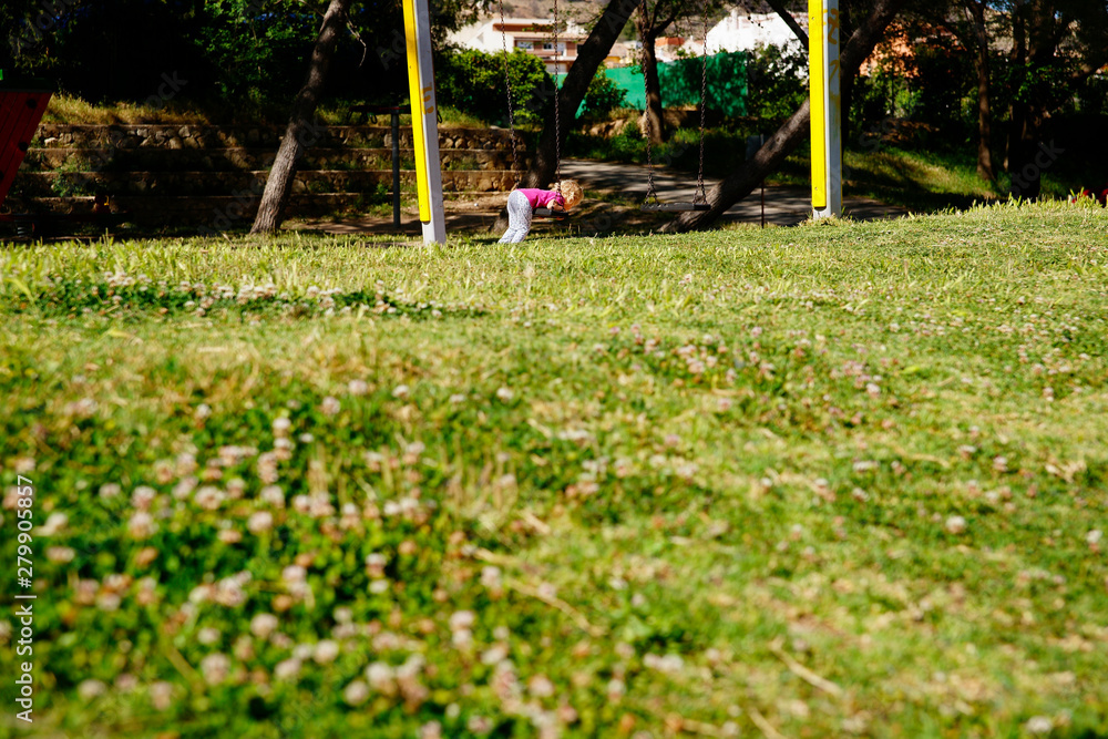 Little girl playing with a swing in a meadow during the summer weekend.