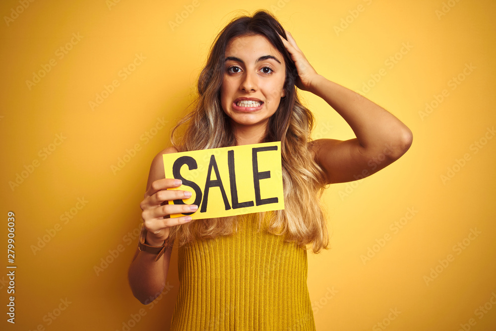 Young beautiful woman holding sale poster over yellow isolated background stressed with hand on head, shocked with shame and surprise face, angry and frustrated. Fear and upset for mistake. Young beautiful woman holding sale poster over yellow isolated background stressed with hand on head, shocked with shame and surprise face, angry and frustrated. Fear and upset for mistake.