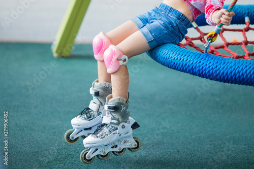 Close up photo of little girl s legs on roller skates at a park. Cheerful preschool girl wearing inline roller skates and protective equipment