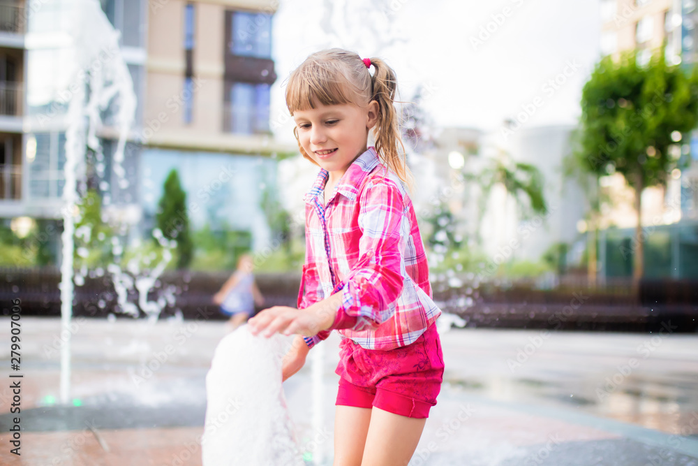 Naklejka premium Little adorable girl having fun in street fountain at hot sunny day