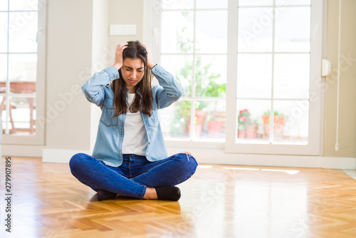 Fotografie Beautiful young woman sitting on the floor at home suffering from headache desperate and stressed because pain and migraine
