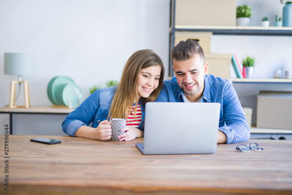 Young couple relaxing drinking a coffee and using the computer laptop around cardboard boxes, very happy moving to a new house Young couple relaxing drinking a coffee and using the computer laptop around cardboard boxes, very happy moving to a new house