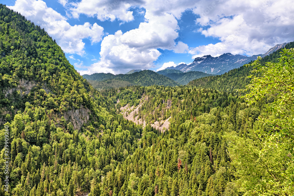 mountain valley panorama landscape against blue sky and dramatic clouds background wide view of green forest in caucasus mountains summer nature beautiful panoramic scenery