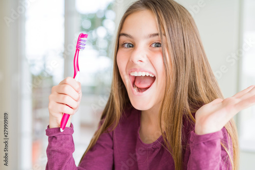 Beautiful young girl kid holding pink dental toothbrush very happy and excited  winner expression celebrating victory screaming with big smile and raised hands