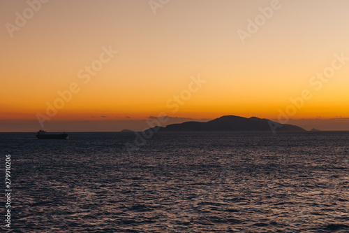 Ship sailing at sunset with island silhouette background and orange sky