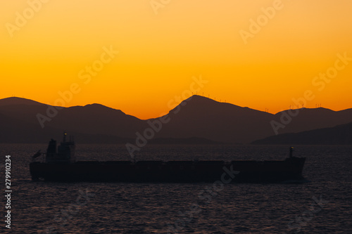 Ship sailing at sunset with island silhouette background and awesome orange sky
