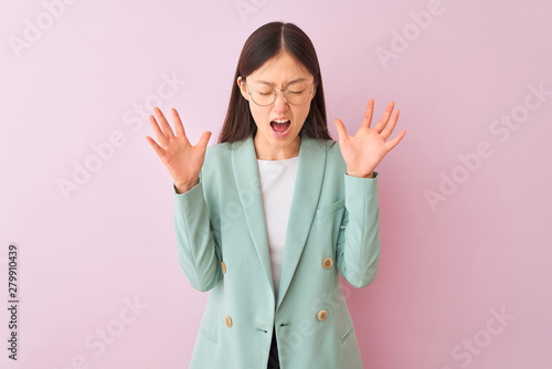 Young chinese businesswoman wearing jacket and glasses over isolated pink background celebrating mad and crazy for success with arms raised and closed eyes screaming excited. Winner concept