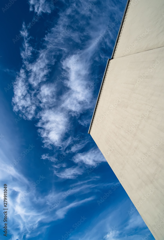 Large flat wall of a modern building without windows against a blue sky with white clouds Large flat wall of a modern building without windows against a blue sky with white clouds