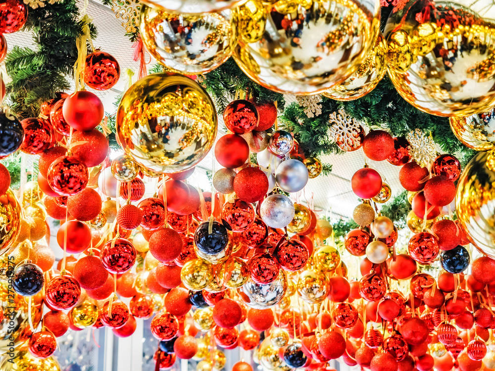Many large golden balls with festooned fir tree garlands and red ribbons are hung indoors. New Year and Christmas tree decorations. Beautiful Christmas background. Street decorations in Europe