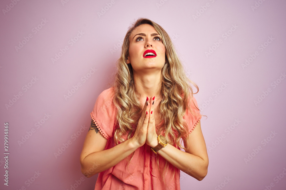Young beautiful woman wearing t-shirt standing over pink isolated background begging and praying with hands together with hope expression on face very emotional and worried. Asking for forgiveness. 