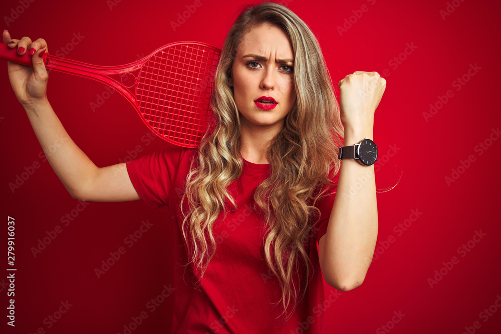 Young sportwoman playing tennis with racket and a ball over red isolated background annoyed and frustrated shouting with anger, crazy and yelling with raised hand, anger concept Young sportwoman playing tennis with racket and a ball over red isolated background annoyed and frustrated shouting with anger, crazy and yelling with raised hand, anger concept
