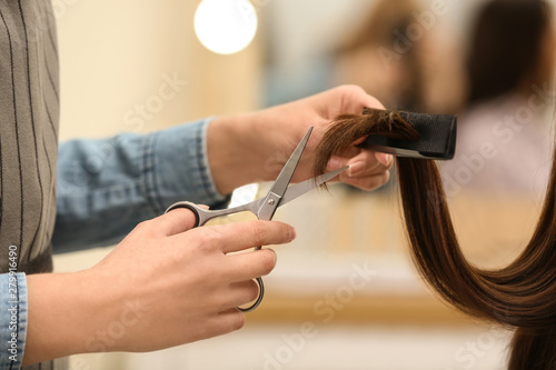 Barber making stylish haircut with professional scissors in beauty salon, closeup