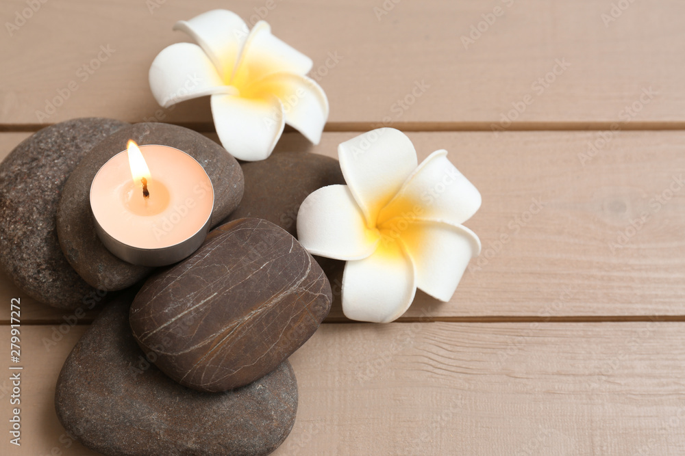 Pile of spa stones with lit candle and flowers on wooden background, space for text Pile of spa stones with lit candle and flowers on wooden background, space for text
