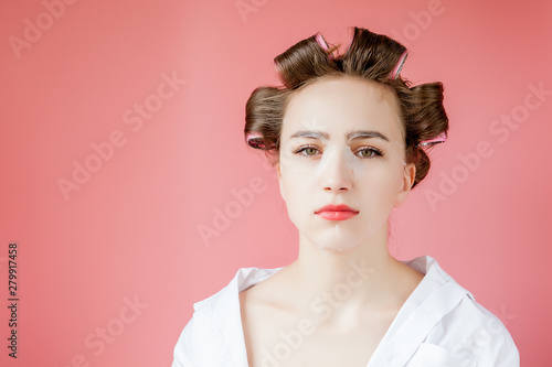 Beautiful young girl with a mask and curlers touching her face.