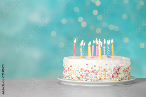 Birthday cake with burning candles on table against light blue background. Space for text