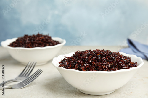 Bowls with delicious cooked brown rice on white table