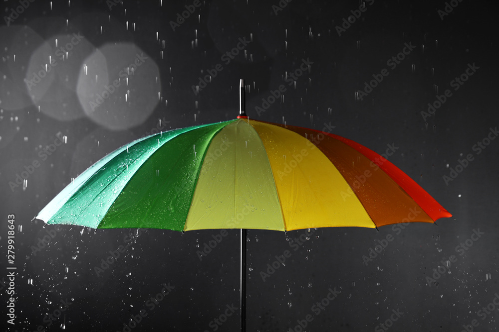 Bright umbrella under rain on dark background