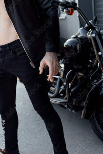 cropped view of man with naked torso holding cigarette and standing not far from motorcycle