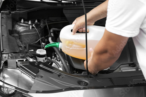 Man pouring liquid from plastic canister into car washer fluid reservoir, closeup